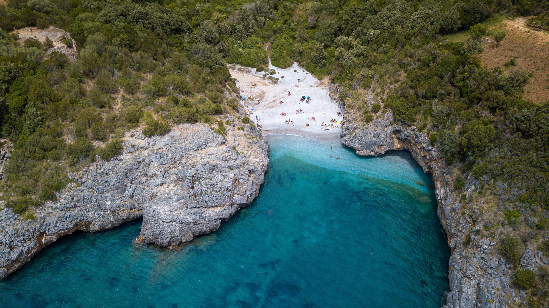 Spiaggia nascosta tra scogli e mare cristallino, circondata da vegetazione rigogliosa.