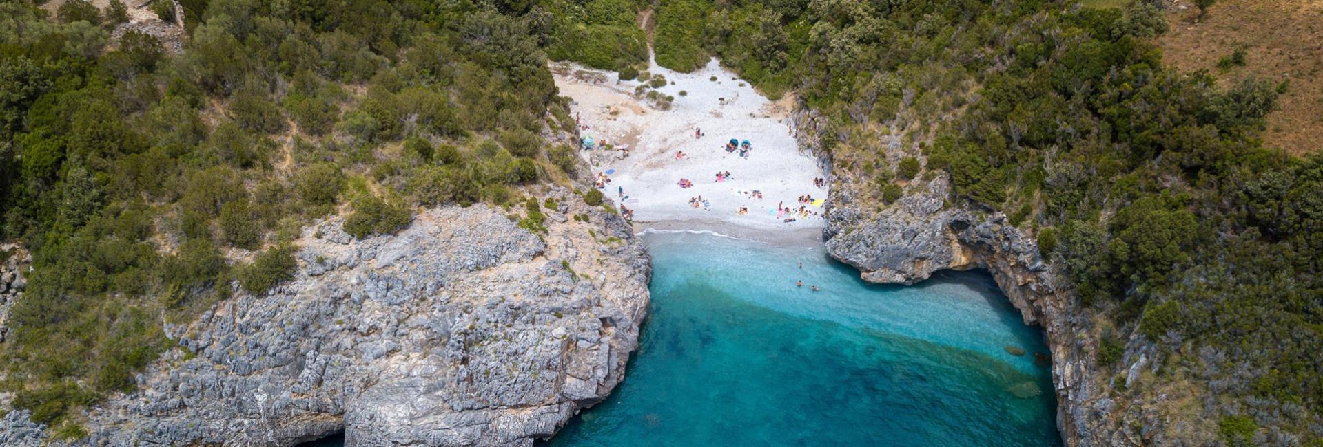 Piccola spiaggia nascosta tra scogli e mare cristallino, circondata da vegetazione verde.