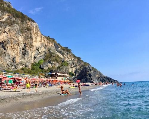 Spiaggia affollata con ombrelloni colorati e mare cristallino, circondata da scogliere imponenti.