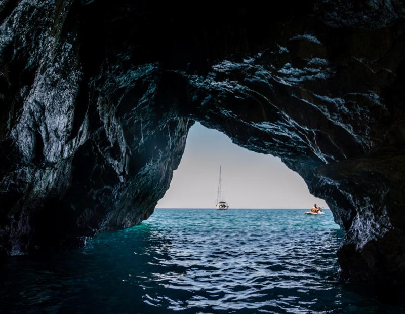 Vista da una grotta sul mare con una barca e un kayak all'orizzonte.